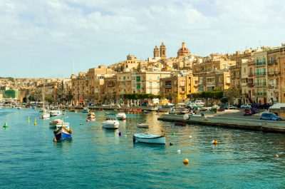 colorful boats in Valletta harbour with view of embankment and cityscape on the background, Malta