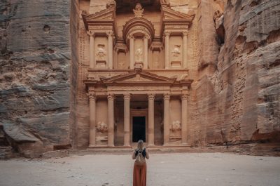 A female in a long orange skirt standing in front of the historic Petra Wadi in Jordan