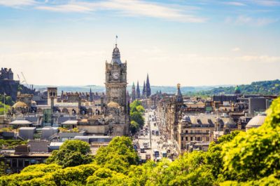 A high angle view over central Edinburgh, with Princes Street busy with pedestrians on a sunny afternoon.